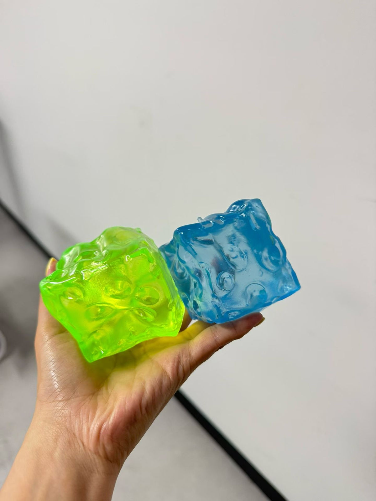 Green and blue crystal ice cube textured squishy fidget toys held in one hand